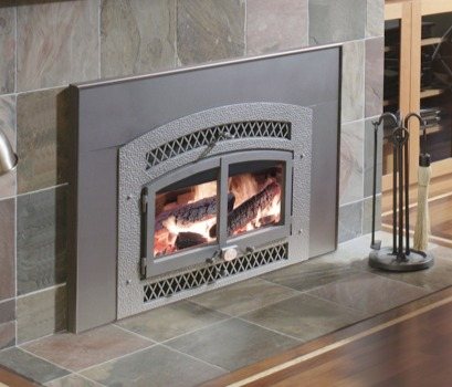 An insert fitted into a tiled fireplace surround with hearth tools alongside